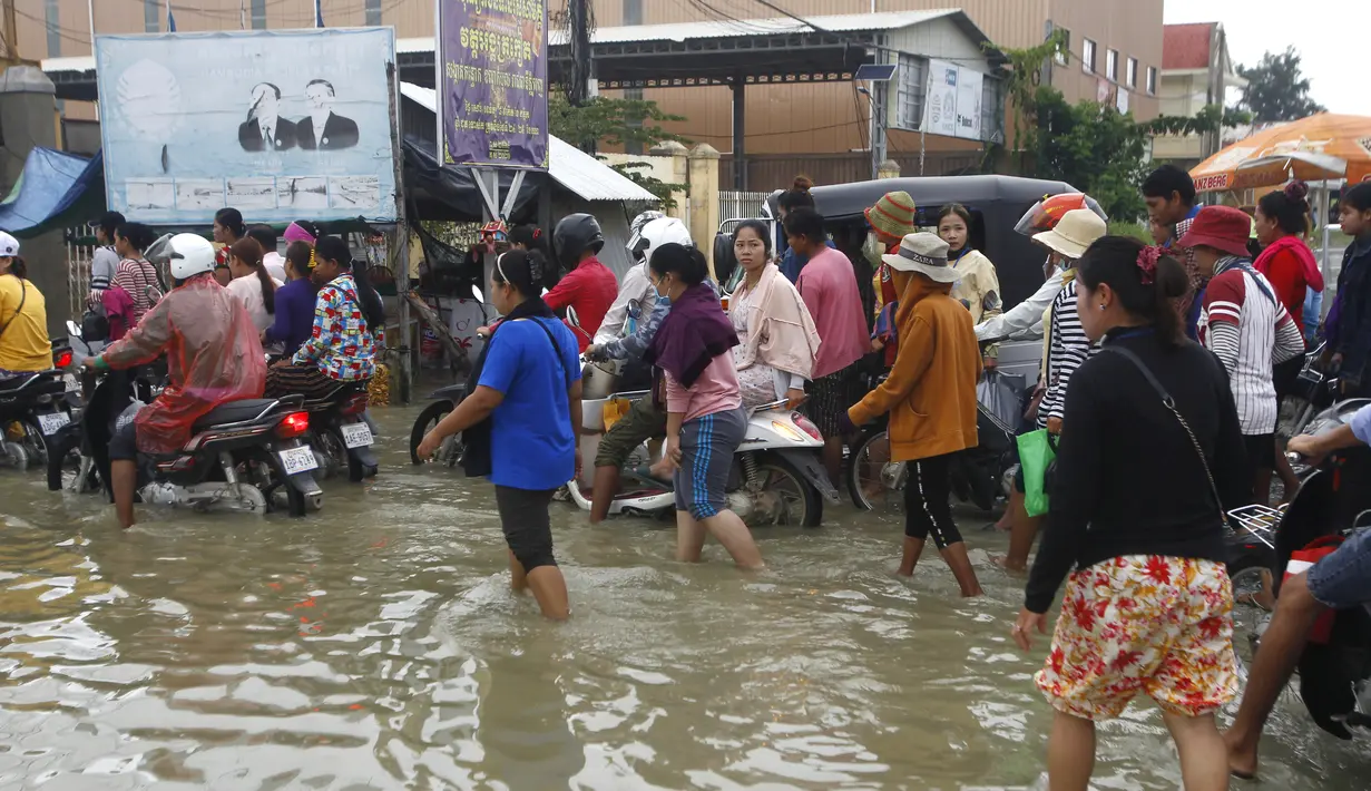 Pekerja garmen pergi ke tempat kerja melalui jalan yang banjir setelah hujan di  Phnom Penh, Kamboja (14 /10/2020). Pejabat bencana Kamboja mengatakan bahwa lebih dari 10.000 orang telah dievakuasi ke tempat aman setelah badai tropis melanda yang menyebabkan banjir bandang.  (AP Photo/Heng Sinith)
