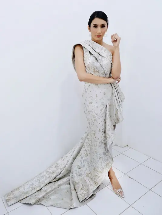 Tyas Mirasih mengenakan gaun one off shoulder berwarna silver rancangan Hazel Kez. Gaun dengan aksen tumpuk di bagian tas dipadukan dengan ruffle di bagian bawah yang memberi kesan glamor pada penampilan Tyas Mirasih.