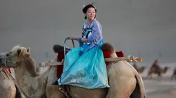 Seorang wanita mengenakan pakaian tradisional menaiki unta di padang pasir di Dunhuang di provinsi Gansu di China barat laut (10/8/2019). Sensus Tiongkok 2000 melaporkan bahwa terdapat 187,578 penduduk di kota tersebut. (AFP Photo/Str)