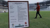 Pekerja melintas di depan papan spesifikasi rumput  di SUGBK, Senayan, Jakarta, Selasa (8/8/2017). SUGBK menggunakan rumput jenis Zoysia matrella yang merupakan rumput standar FIFA untuk stadion bertaraf internasional. (Bola.com/M Iqbal Ichsan)