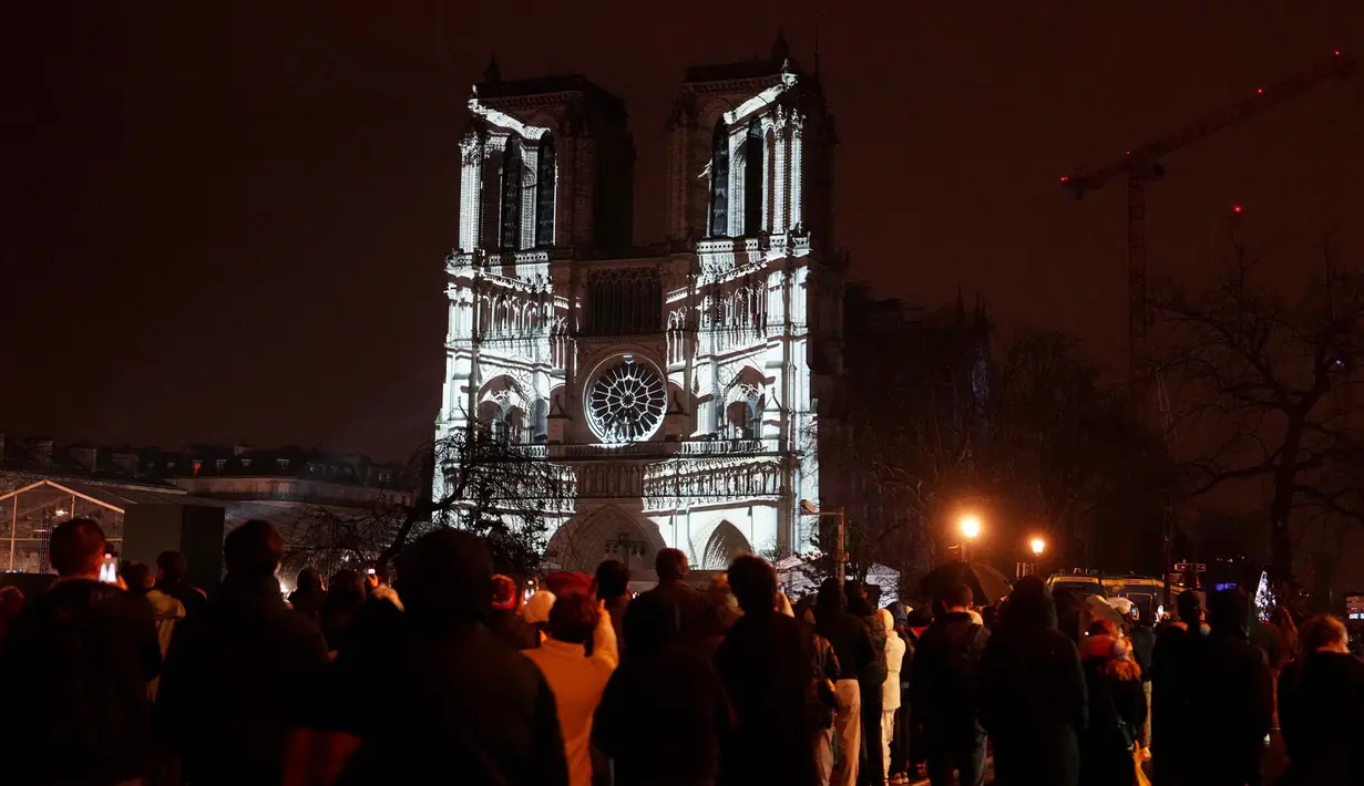 Kerumunan orang berdiri di luar Katedral Notre-Dame yang diterangi lampu saat upacara yang menandai pembukaan kembali katedral yang menjadi ikon kota Paris ini, di pusat kota Paris, pada tanggal 7 Desember 2024. (Dimitar DILKOFF/AFP)