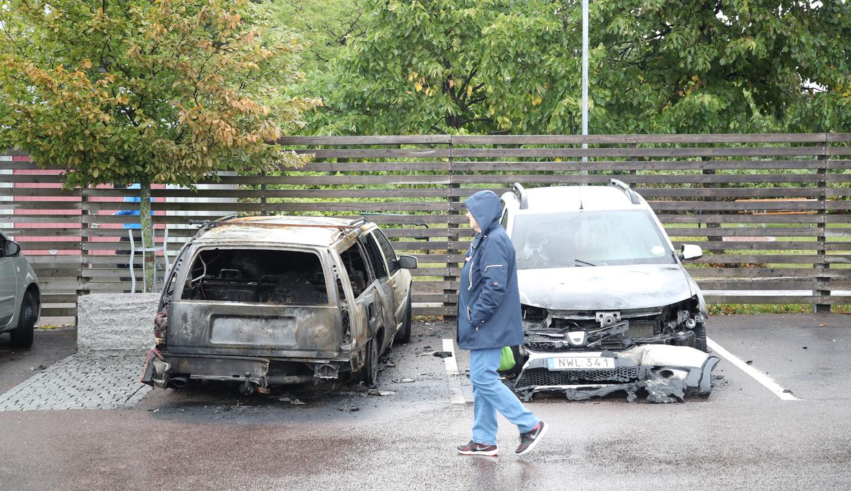 Pejalan kaki melintasi mobil yang hangus terbakar oleh orang tak dikenal di kota Gothenburg, Swedia, Selasa (14/8). Aksi vandalisme besar-besaran ini juga terjadi menjelang pemilu yang digelar pada 9 September ini. (Henrik BRUNNSGARD/TT News Agency/AFP)