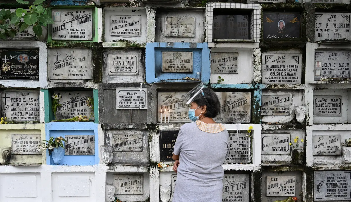 Seorang wanita berdoa di depan makam seorang kerabat di sebuah pemakaman di Manila, Filipina (28/10/2021). Pemerintah setempat akan menutup pemakaman nasional untuk Hari Semua Orang Kudus karena pandemi virus corona Covid-19. (AFP/Ted Aljibe)