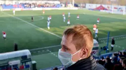 Suporter menggunakan masker saat menonton pertandingan antara FC Minsk melawan FC Dinamo-Minsk pada laga Liga Belarusia, Sabtu (28/3/2020). Di tengah wabah virus Corona, Liga Belarusia tetap digelar seperti biasa bahkan tetap dipadati suporternya. (AFP/Sergei Gapon)