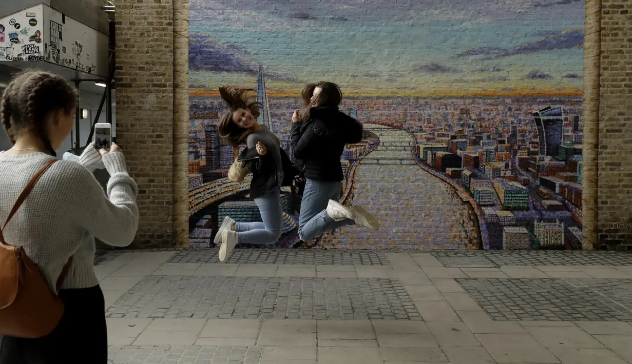 Orang yang lewat berpose untuk foto setelah seniman jalanan Australia James Cochran, juga dikenal sebagai Jimmy C menyelesaikan mural lanskap kota London di dinding Network Rail oleh Blackfriars Station, di London (5/10/2020). (AP Photo/Matt Dunham)