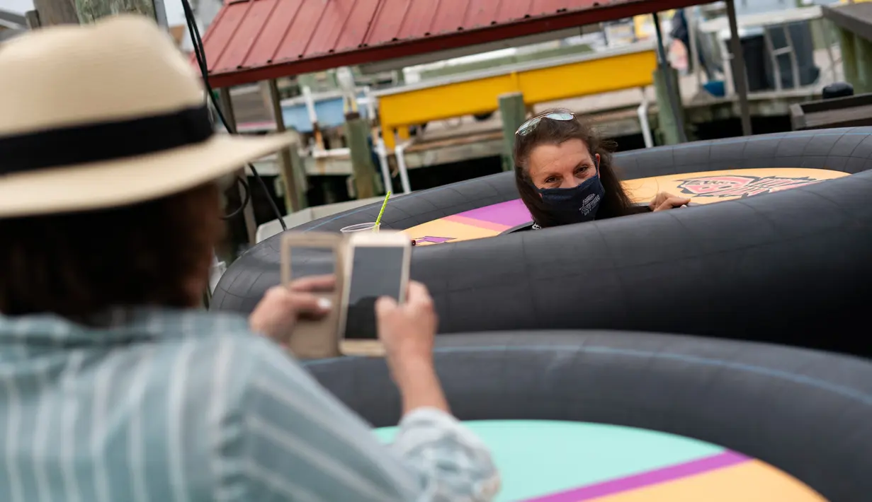 Para tamu mencoba meja portabel yang bentuknya menyerupai ban pelampung untuk menjaga jarak pelanggan di Fish Tales Bar & Grill di Ocean City, Maryland, Jumat (29/5/2020). Pengunjung akan berdiri di bagian tengah meja bundar itu yang dilengkapi roda untuk memudahkan pergerakan. (Alex Edelman/AFP)
