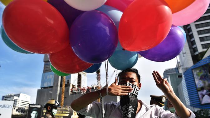 Seorang pengunjuk rasa memegang seikat balon sambil memberi hormat pada Hunger Games dengan tiga jari selama protes terhadap usulan pembelian kapal selam oleh Perdana Menteri Thailand Prayut Chan-O-Cha yang berpihak pada militer di Bangkok (31/8/2020). (AFP/Lillian Suwanrumpha)