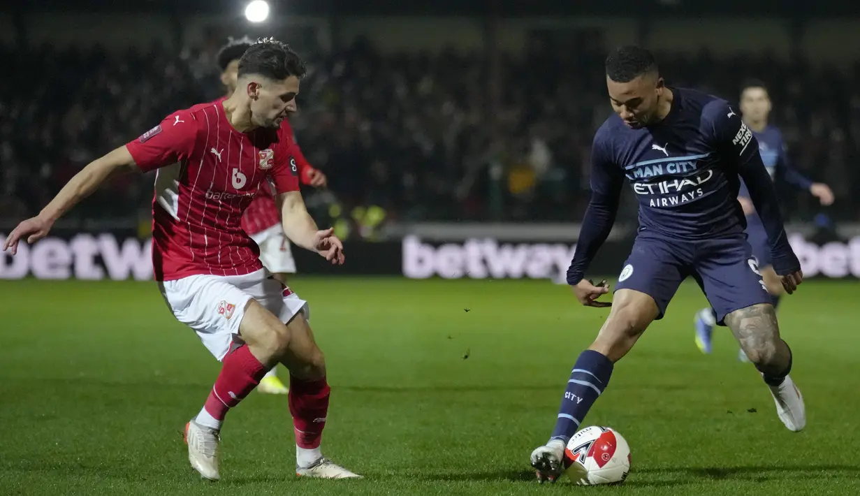 Bek tim divisi 4 Swindon Town, Rob Hunt berebut bola dengan penyerang Manchester City Gabriel Jesus dalam duel putaran ketiga Piala FA 2021/22 di County Ground, Sabtu (8/1/2022) dini hari WIB. Manchester City menang telak 4-1 saat menghadapi Swindon Town. (AP Photo/Kirsty Wigglesworth)
