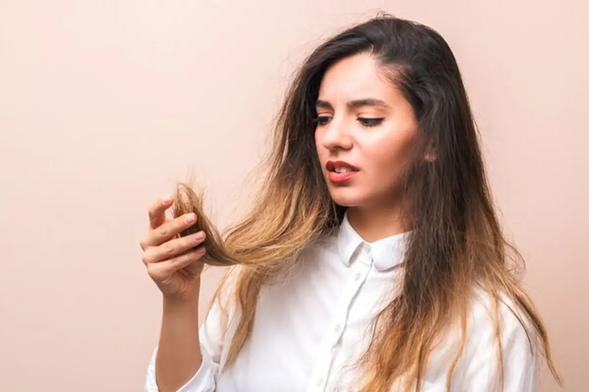Seorang perempuan berbaju putih sedang memegang rambutnya yang tampak kering dan rusak (Foto Dok: Freepik/user15503477)