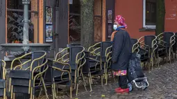 Seorang wanita mengenakan masker saat melewati teras kosong di kawasan Marrolles di Brussels, Rabu (17/11/2021). Pemerintah Belgia mewajibkan kembali penggunaan masker dan memberlakukan warga bekerja dari rumah dalam upaya untuk menahan lonjakan baru kasus COVID-19. (AP Photo/Olivier Matthys)