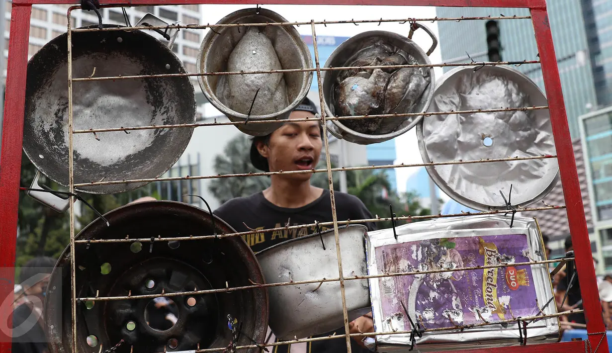 Seorang mahasiswa yang tergabung dalam Kreasi Musik Mahasiswa IISIP (Kremmasi) memukul panci dan alat masak lainnya saat memainkan alat musik dari barang bekas di kawasan Bundaran HI, Jakarta, Minggu (14/5). (Liputan6.com/Immanuel Antonius)