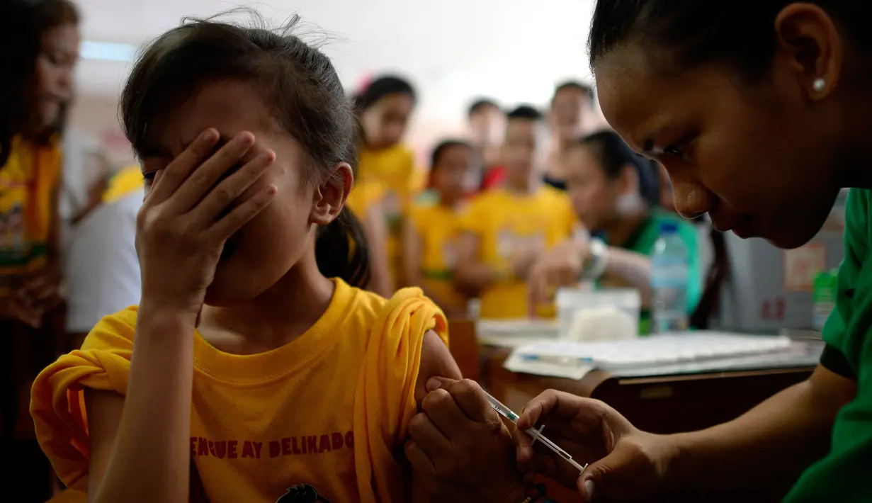Siswi menutup mukanya saat petugas menyuntikkan vaksin anti-dengue di Sekolah Dasar Parang di Marikina, sebelah barat Manila, Senin (4/4). Filipina telah menyuntikkan vaksin pertama di dunia untuk penyakit DBD itu kepada 1 juta pelajar. (NOEL CELIS/AFP)