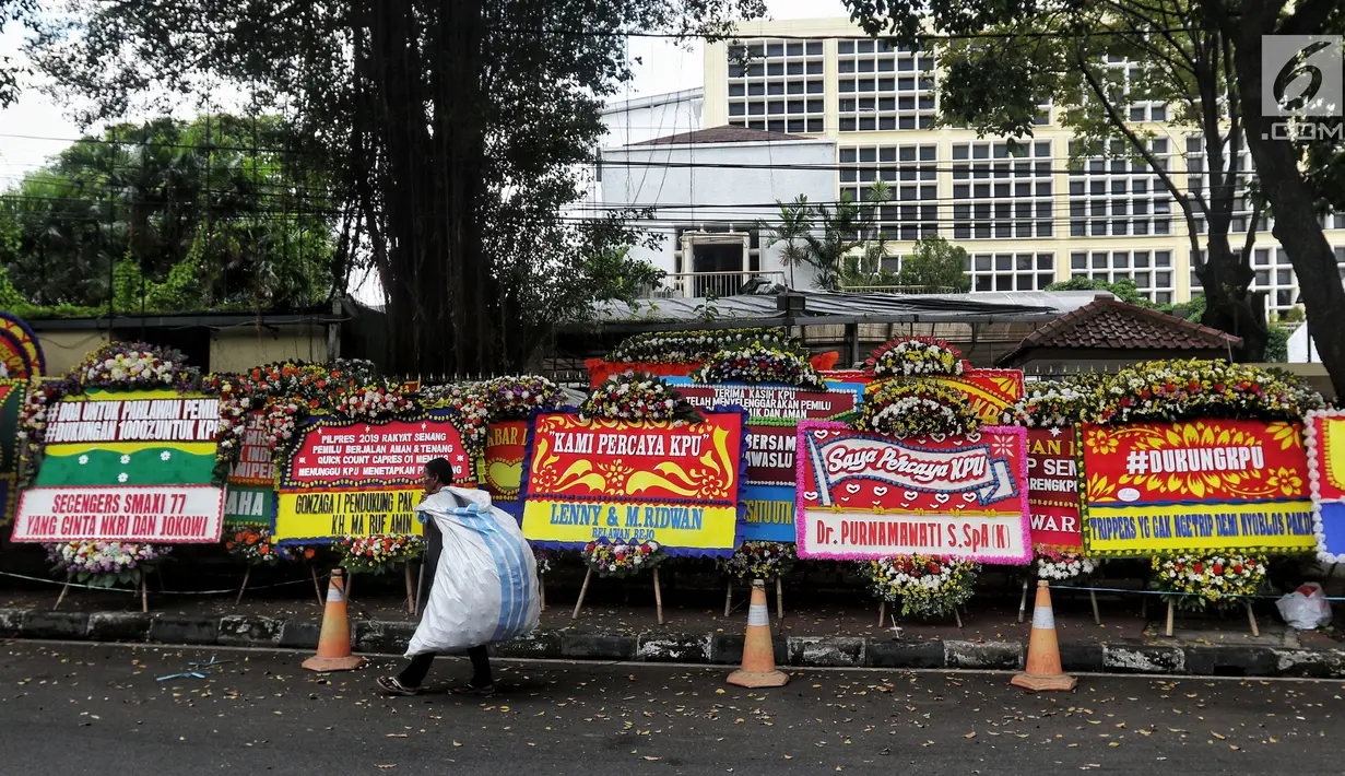 Pemulung berjalan melewati karangan bunga di depan Gedung KPU, Jakarta, Sabtu (21/4). Karangan bunga di depan Gedung KPU terus bertambah setiap harinya. (Liputan6.com/JohanTallo)