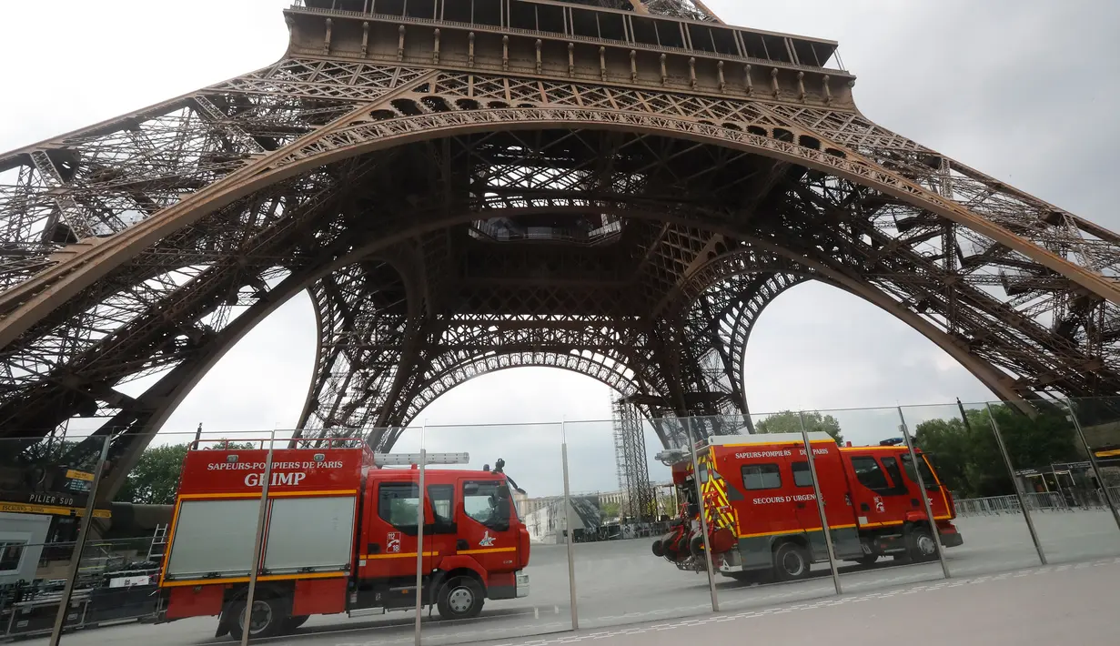 Kendaraan petugas penyelamat terparkir di bawah Menara Eiffel, Paris, Senin (20/5/2019). Menara Eiffel ditutup bagi pengunjung setelah seseorang pria berusaha memanjat bangunan ikonik tersebut tanpa izin. (AP/Michel Euler)