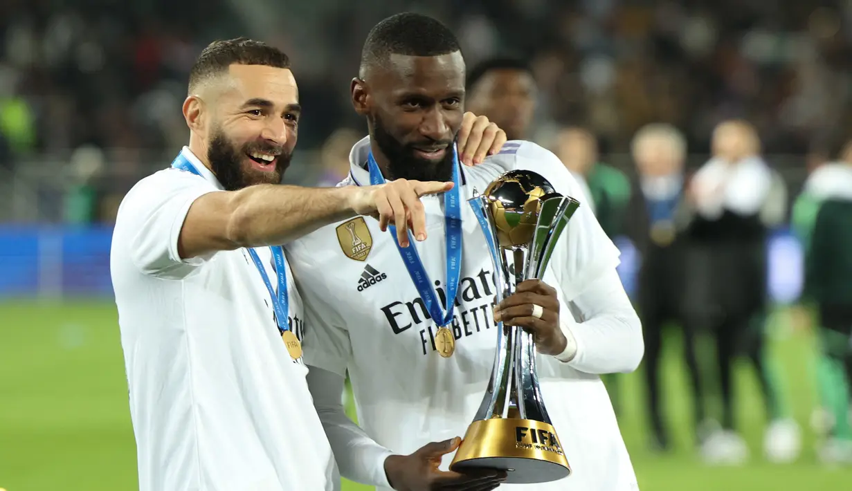 Penyerang Real Madrid Karim Benzema (kiri) dan bek Antonio Rudiger berselebrasi sambil memegang trofi Piala Dunia Antarklub 2022 usai mengalahkan Al Hilal dalam laga final di Prince Moulay Abdellah Stadium, Rabat, Minggu (12/2/2023) dini hari WIB. Los Blancos pun memegang rekor sebagai klub dengan gelar Piala Dunia Antarklub terbanyak. (FADEL SENNA / AFP)