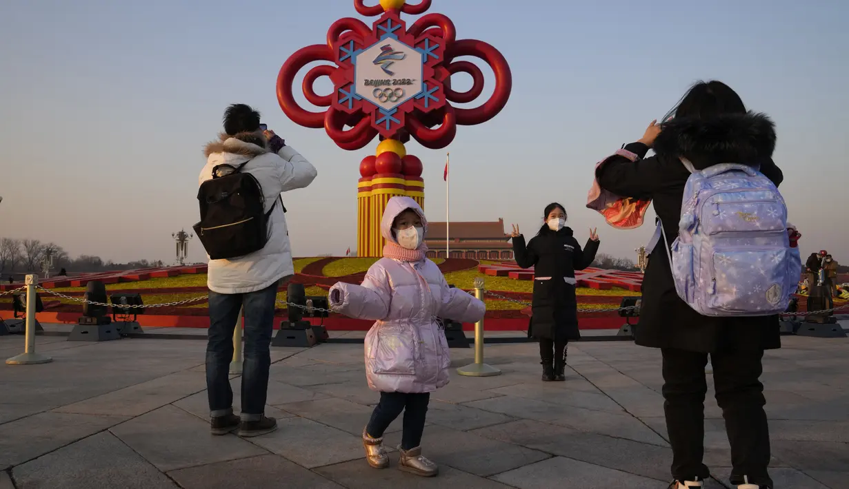 Warga yang mengenakan masker untuk melindungi diri dari virus corona berpose di depan dekorasi Olimpiade Musim Dingin Beijing di Lapangan Tiananmen di Beijing, China (18/1/2022). China telah mengunci sebagian distrik Haidian Beijing menyusul deteksi tiga kasus. (AP Photo/Ng Han Guan)