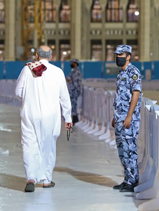 Petugas keamanan Saudi berjaga-jaga saat orang Saudi dan ekspatriat melakukan sholat "Al Fajr" di Masjidil Haram di kota suci Mekkah (18/10/2020). Saudi juga memperbolehkan umrah untuk menampung 15.000 jamaah karena melonggarkan pembatasan virus corona. (AFP/STR)