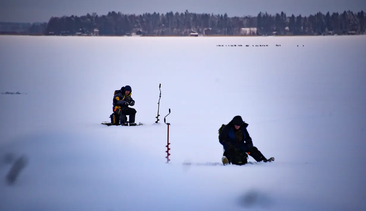Dua orang pria memancing di tengah laut Bothnia yang sedang membeku di Vaasa, Finlandia, Rabu (27/12). Memancing di laut beku merupakan hal yang ditunggu-tunggu oleh sebagian warga setempat. (OLIVIER MORIN / AFP)