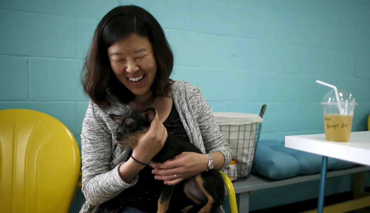 Pengunjung bermain dengan seekor anjing sambil menikmati minumannya saat pembukaan Dog Cafe coffee shop di Los Angeles, AS (7/4). Anjing di kafe ini juga dapat diadopsi oleh pengunjung sebagai peliharaan yang dilindungi. (REUTERS/Lucy Nicholson)