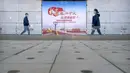 Orang-orang yang mengenakan masker melewati papan reklame yang menandai Kongres Nasional ke-20 Partai Komunis China yang akan datang, di Beijing, Selasa (11/10/2022). Kota-kota di China memberlakukan kembali lockdown dan pembatasan perjalanan. (AP Photo/Mark Schiefelbein)