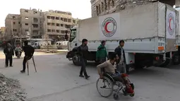 Orang-orang lalu lalang di sekitar truk bantuan yang memasuki wilayah Douma, Ghouta Timur, Damaskus, Suriah, Senin (5/3). Badan Urusan Pengungsi PBB atau UNHCR mengatakan, konvoi terdiri dari 46 truk. (AFP PHOTO/AMER ALMOHIBANY)