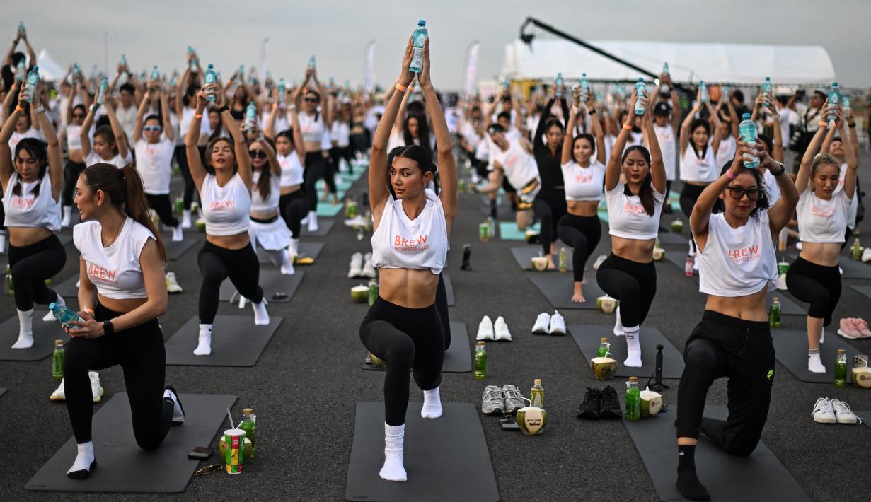 Para penggemar yoga melakukan yoga selama acara "Brew Yoga" saat matahari terbit di landasan pacu Bandara Suvarnabhumi di Bangkok, Thailand, Sabtu (27/4/2024). (MANAN VATSYAYANA / AFP)