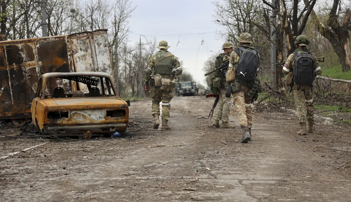 Prajurit milisi Republik Rakyat Donetsk berjalan melewati kendaraan yang rusak selama pertempuran sengit di daerah yang dikendalikan oleh pasukan separatis yang didukung Rusia di Mariupol, Ukraina, Selasa (19/4/2022).  (AP Photo/Alexei Alexandrov)