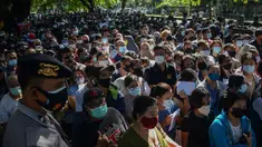 Polisi melakukan pengamanan saat warga menunggu dalam antrean untuk mendaftar vaksin virus corona COVID-19 AstraZeneca di Denpasar, Bali, Sabtu (26/6/2021). Ratusan warga terlihat antusias mengikuti vaksinasi massal ini. (SONY TUMBELAKA/AFP)