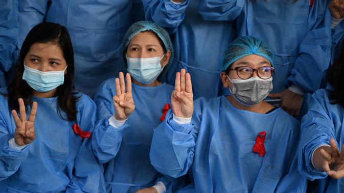 Tenaga medis mengenakan pita merah di seragamnya memberi hormat tiga jari di Rumah Sakit Umum Yangon di Yangon (3/2/2021). Mereka tidak akan menghentikan gerakan ini sampai pemerintahan terpilih dipulihkan. (STR / AFP)