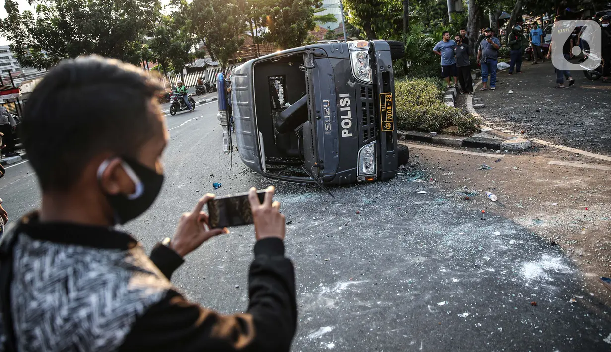 Seorang pria mengambil gambar sebuah mobil polisi yang dirusak massa saat bentrok di kawasan Pejompongan, Jakarta, Rabu (7/10/2020). (Liputan6.com/Faizal Fanani)
