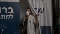 Pekerja medis Clalit Health Services mengintip dari stannya saat memanggil pasien berikutnya untuk divaksin covid-19 di Yerusalem, Senin (3/1/2022). Israel menyetujui pemberian dosis booster tersebut kepada kelompok warga berusia di atas 60 tahun dan tenaga medis. (AP Photo/Maya Alleruzzo)