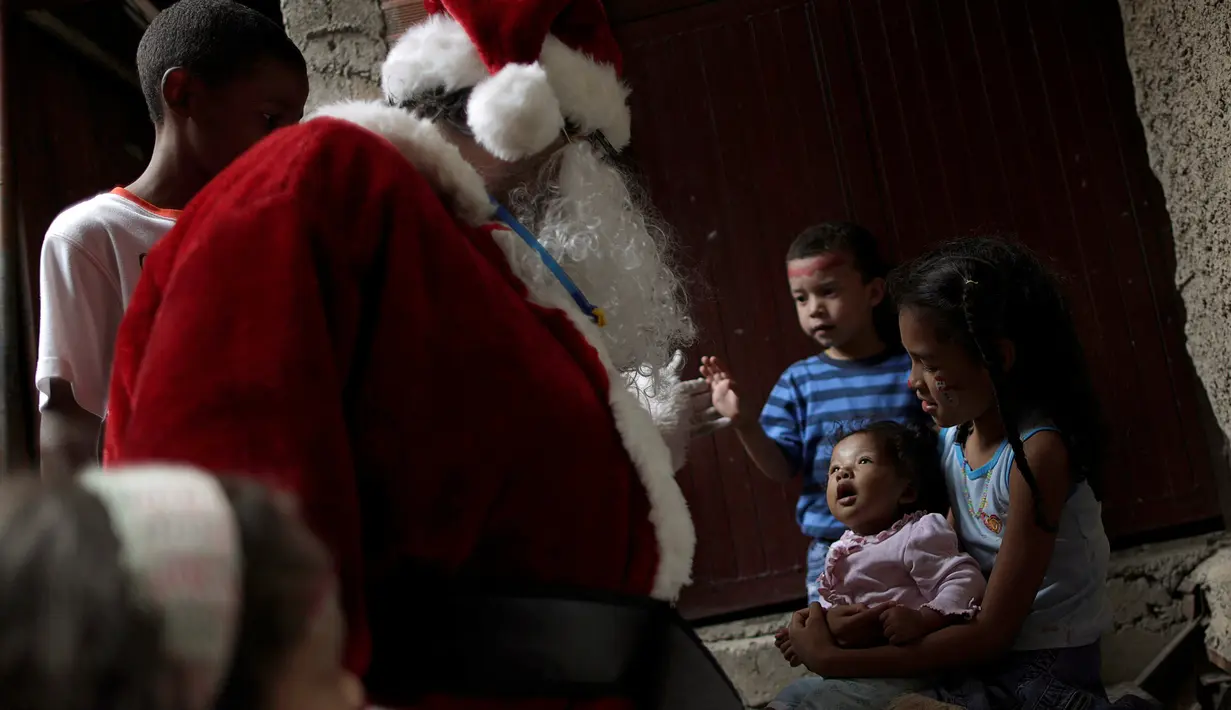 Santa Claus menghibur seorang balita saat mengunjungi kawasan kumuh Petare di Caracas, Venezuela (11/12). Kunjungan Santa Claus ini untuk menghibur anak-anak Petare dalam menyambut datangnya natal. (Reuters/Ueslei Marcelino)