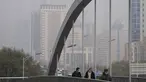 Orang-orang yang memakai masker untuk membantu mengekang penyebaran virus corona berjalan di atas jembatan di atas gedung perkantoran yang diselimuti kabut polusi di Beijing, Kamis (18/11/2021).  (AP Photo/Andy Wong)