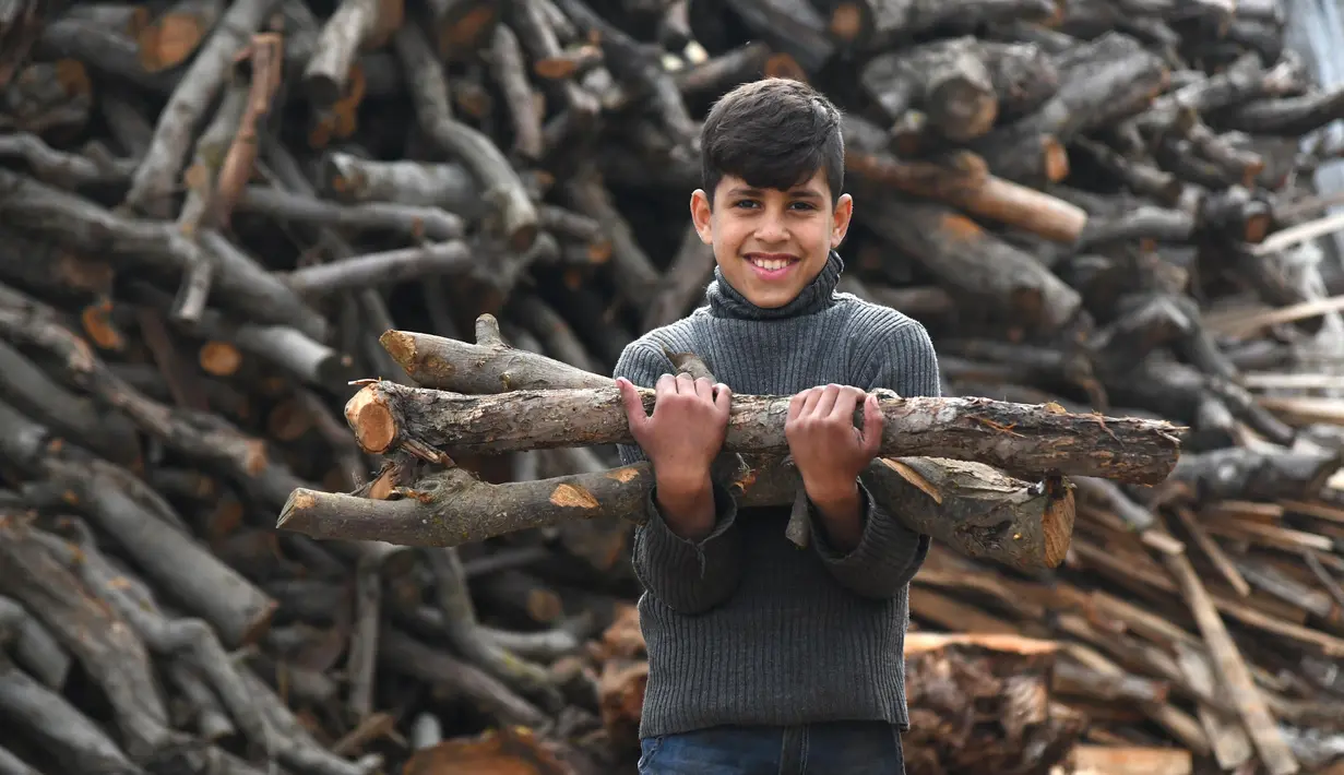 Seorang anak laki-laki menggotong kayu bakar di sebuah bengkel kerja di Damaskus, ibu kota Suriah, pada 23 November 2020. Warga Suriah mengumpulkan kayu bakar untuk menghadapi cuaca dingin. (Xinhua/Ammar Safarjalani)