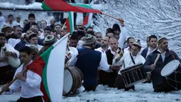 Sejumlah pria Bulgaria mengibarkan bendera sambil memainkan alat musik tradisional sambil menari di perairan sungai Tundzha selama Hari Epiphany di kota Kalofer, Bulgaria (6/1). (AP Photo/Valentina Petrova)