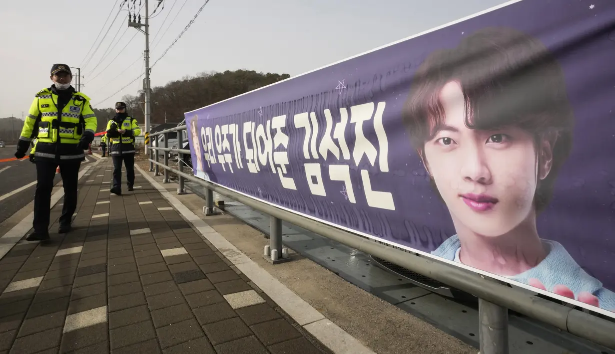 Petugas polisi Korea Selatan melewati spanduk yang menunjukkan gambar member grup K-Pop BTS, Jin di dekat pusat pelatihan tentara di Yeoncheon, Selasa (13/12/2022). Kim Seok-jin atau yang lebih dikenal dengan nama Jin BTS memulai wajib militer pada hari Selasa 13 Desember 2022 ini. (AP Photo/Ahn Young-joon)
