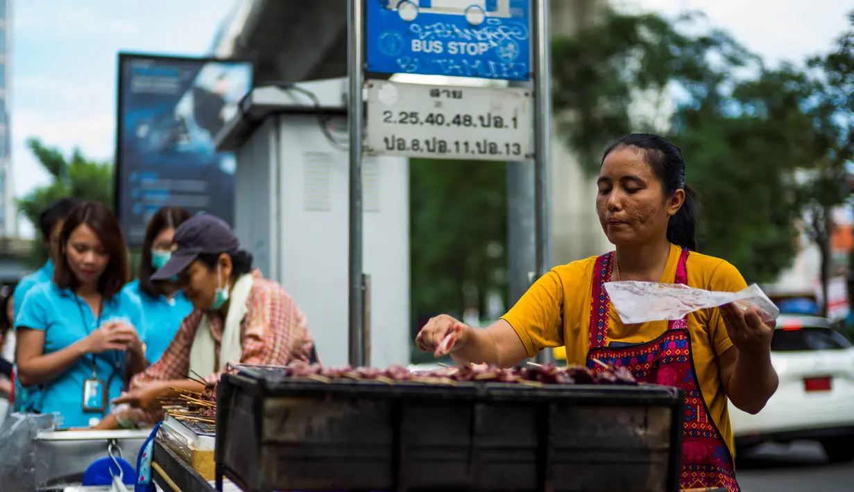 Seorang wanita memasak sate di gerobaknya di samping jalan di Bangkok, Thailand (20/9). (AFP Photo/Jewel Samad)