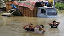 Warga menyeberangi truk yang terendam banjir saat banjir di Lhoksukon, Aceh Utara, Aceh, 3 Januari 2022. Badan Penanggulangan Bencana Daerah (BPBD) Aceh Utara mencatat banjir telah merendam 14 kecamatan di daerah tersebut. (AZWAR IPANK/AFP)