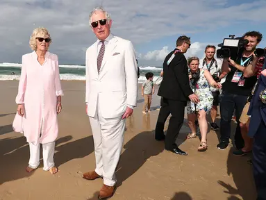 Pangeran Charles bersama istrinya, Duchess of Cornwall Camilla berjalan di atas pasir pantai saat mengunjungi Broadbeach di Gold Coast, Australia, Kamis (5/4). Istri Pangeran Charles itu terlihat berjalan tanpa alas kaki. (Mark Metcalfe/POOL/AFP)