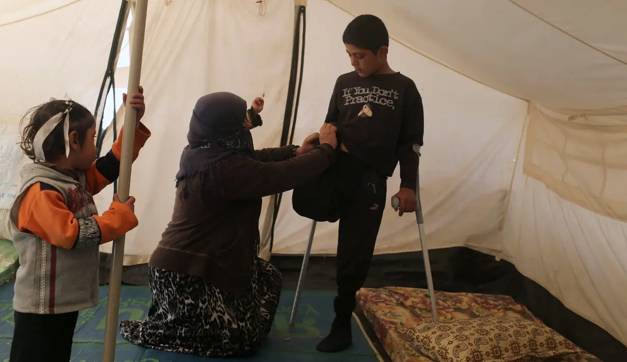 Jasim Abudllah dibantu ibunya mengenakan celana di kamp Debaga, di pinggiran Erbil, Irak (24/11). Bocah berumur 13 tahun tersebut, terpaksa harus kehilangan kaki kanannya akibat terkena serangan udara di Baiji. (Reuters/Mohammed Salem)
