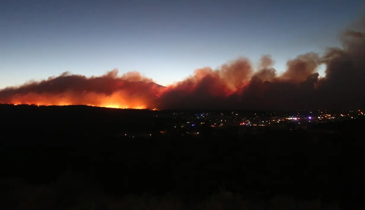 <p>Kebakaran hutan yang membakar memancarkan cahaya di atas lingkungan di pinggiran Flagstaff, Arizona, Minggu (12/6/2022). Evakuasi telah diperintahkan untuk rumah-rumah di daerah tersebut. Pihak berwenang mengatakan petugas pemadam kebakaran menanggapi kebakaran hutan sekitar enam mil di utara Flagstaff yang telah memaksa evakuasi. (AP Photo/Felicia Fonseca)</p>