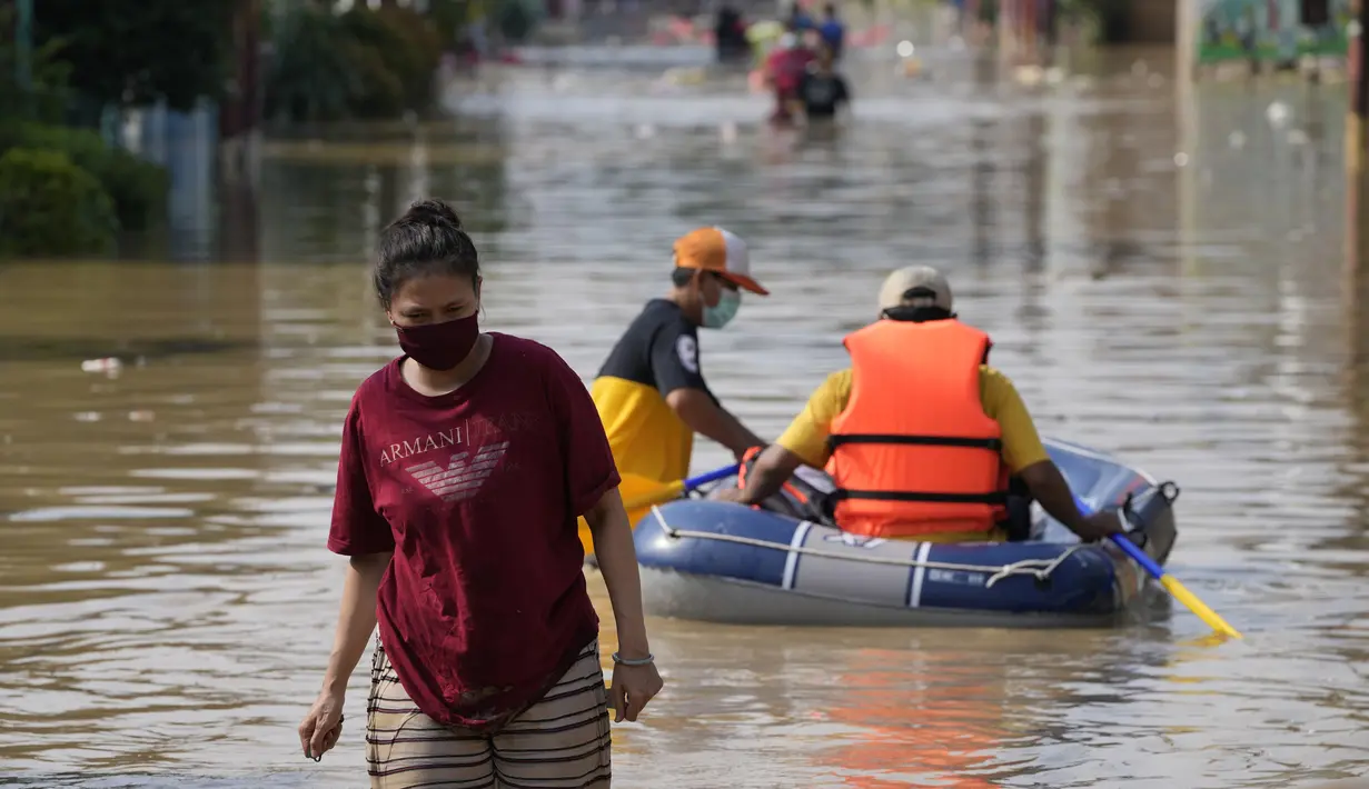 Seorang wanita mengarungi jalan yang banjir di Bekasi, Jawa Barat, Kamis (17/2/2022). Hujan deras yang dikombinasikan dengan perencanaan pembuangan limbah kota yang buruk sering menyebabkan banjir besar. (AP Photo/Achmad Ibrahim)