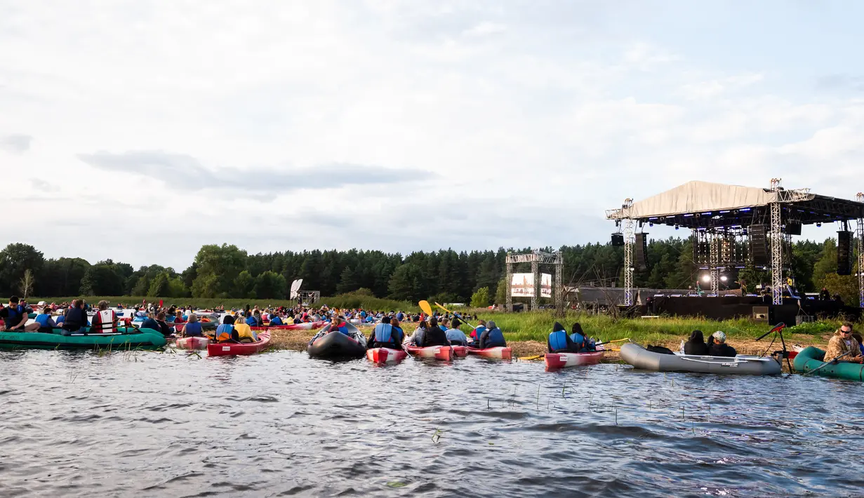Para penonton menikmati konser musik Laivā dari atas perahu di Danau Juglas, Riga, Latvia, 14 Agustus 2021. Warga Latvia bisa menikmati konser musik dari atas kayak, sampan, dan kapal motor bahkan ketika mereka belum divaksin COVID-19. (Gints Ivuskans/AFP)