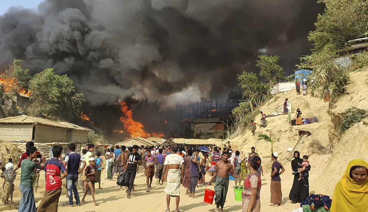 Pengungsi Rohingya menyaksikan asap membubung menyusul kebakaran di kamp pengungsi Rohingya di Balukhali, Bangladesh selatan (22/3/2021). Sejumlah orang meninggal dan 20 ribu orang mengungsi akibat kebakaran hebat di kamp pengungsi. (AP Photo/Shafiqur Rahman)
