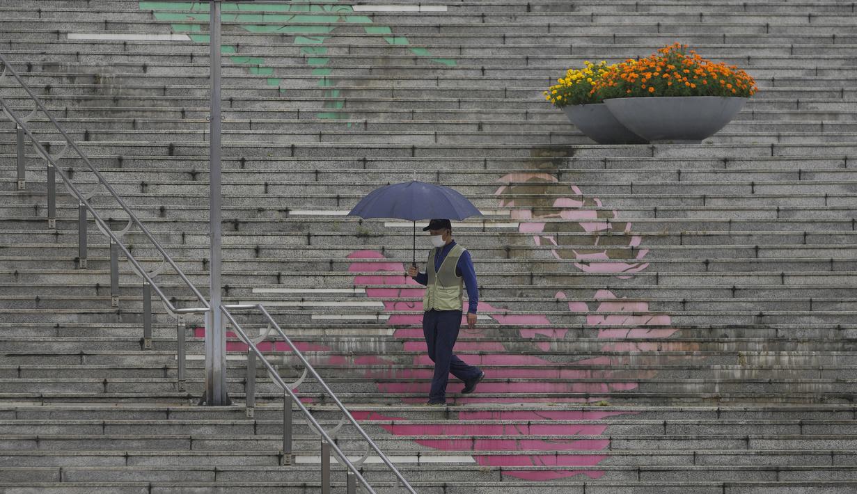 Seorang pria yang mengenakan masker untuk membantu mengekang penyebaran virus corona memegang payung di tengah hujan di Seoul, Korea Selatan, Selasa (31/8/2021). (AP Photo/Lee Jin-man)