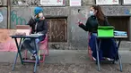 Anita Iacovelli (kiri) dan temannya Lisa Rogliatti, berusia 12 tahun, duduk di depan sekolah Italo Calvino di Turin, Italia, 17 November 2020. Anita memprotes penutupan sekolahnya karena pembatasan COVID-19 dengan duduk di luar gedung sambil mengikuti pelajaran jarak jauh. (Miguel MEDINA/AFP)