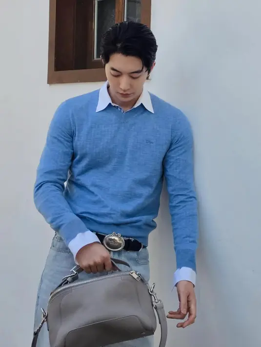 Nam Joo Hyuk tampil dengan inner kemeja dipadukan outer sweater baby blue dan celana denim sambil membawa Dior Archie Bag abu-abu. [@skawngur]