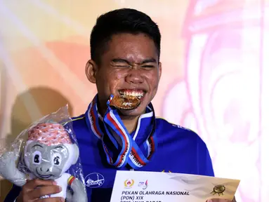 Karateka Jawa Barat, Rahmad menggigit medali usai memenangi laga final Kata Putra Perorangan PON XIX di GOR Sabuga, Bandung, Minggu (18/9). Di final, Rahmad berhasil mengungguli karateka Jambi, Erlando Stevano. (Liputan6.com/Helmi Fithriansyah)