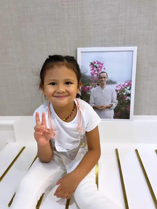Tak bertemu Reza Gunawan, Sea tak kehabisan akal untuk bisa berpose sang paman. Ia pun duduk di sebuah tempat dengan latar belakang foto Reza. Sea tampak tersenyum. (Foto: Instagram/@mrssharena)