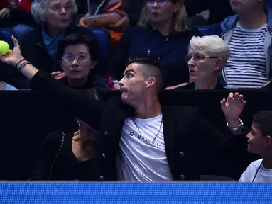 Pemain Juventus, Cristiano Ronaldo menangkap bola tenis yang mengarah kepadanya dan sang kekasih, Georgina saat menyaksikan Novak Djokovic menghadapi John Isner pada laga tenis dunia, ATP Finals 2018, di O2 Arena, London, Senin (12/11). (Glyn KIRK/AFP)